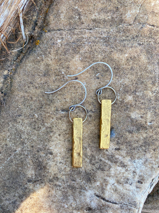 Gold bar earrings on a textured stone surface