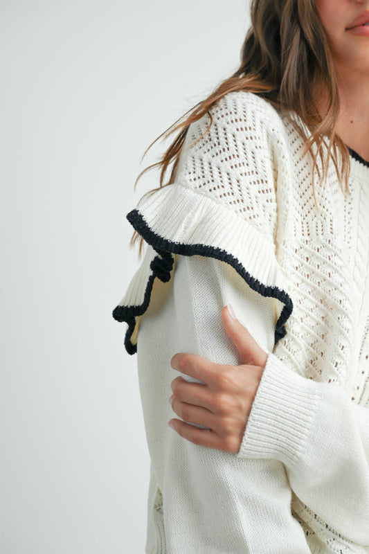 A woman wearing a white sweater with ruffled shoulders and black jeans.