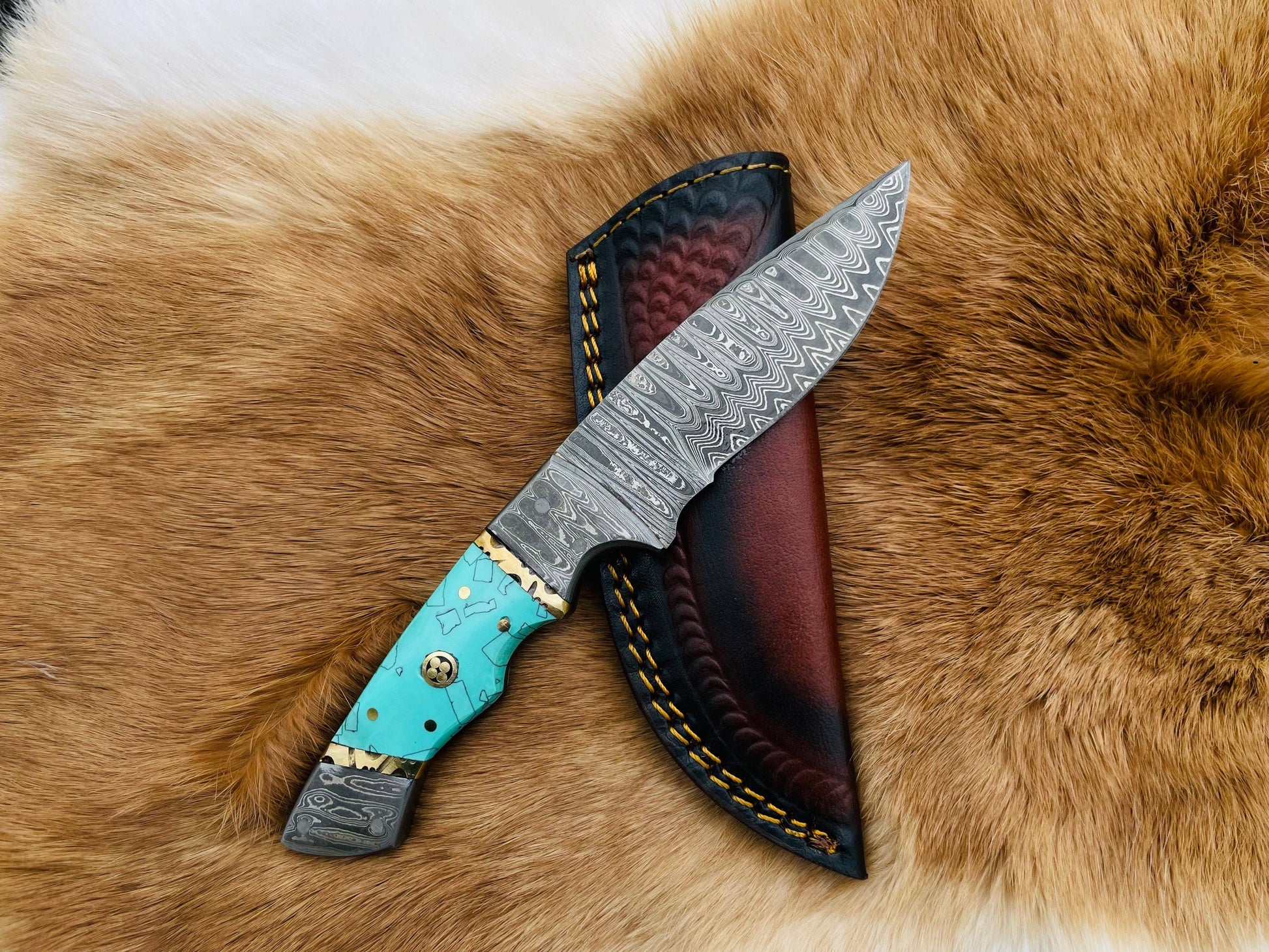 A folding utility knife with a Damascus steel blade and a turquoise resin grip handle, displayed on a brown fur surface.