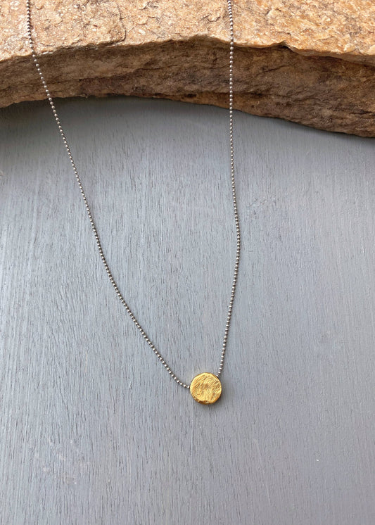 Gold pendant necklace on a gray surface with a stone background