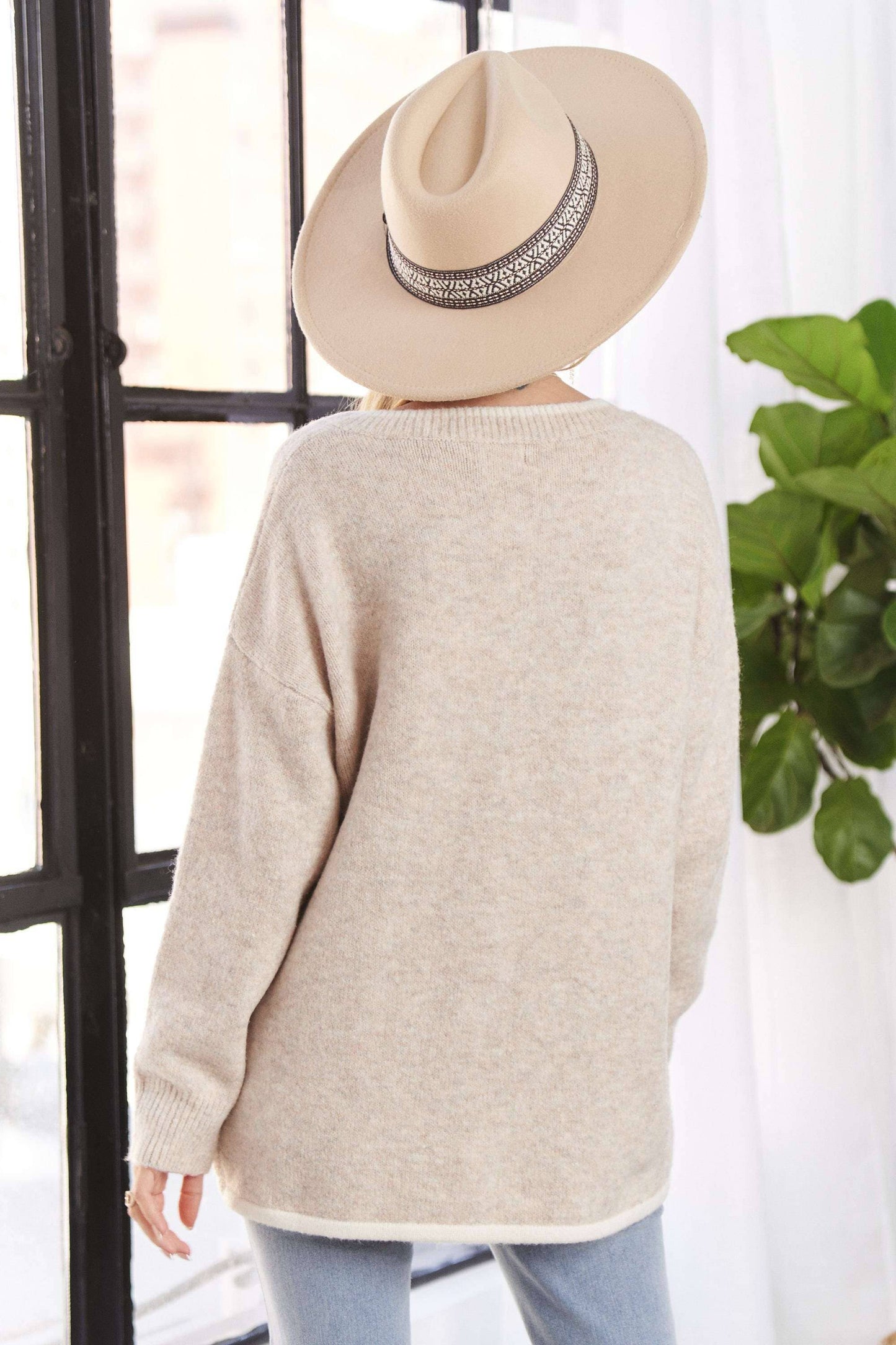 Person wearing a beige sweater and hat with a plant in the background