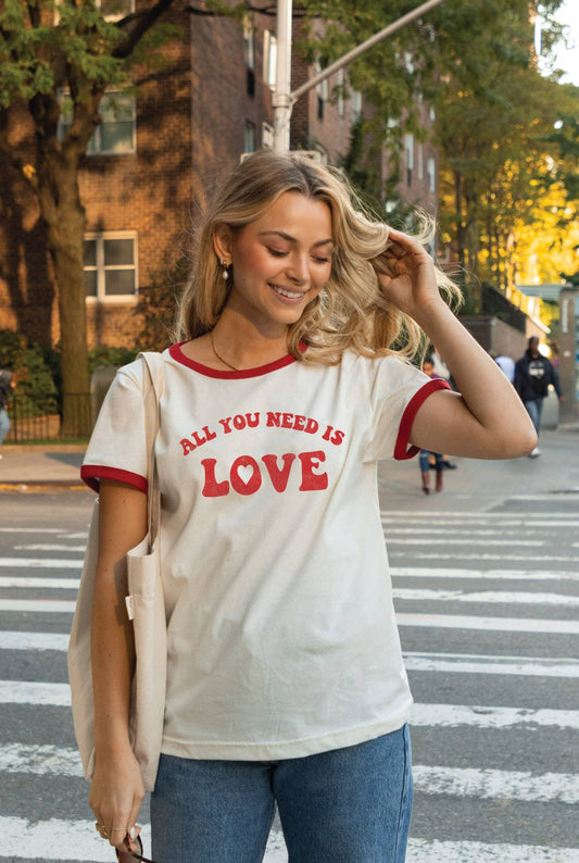 A ringer t-shirt with a white body and yellow collar, with the text 'ALL YOU NEED IS LOVE' printed in red on the front.